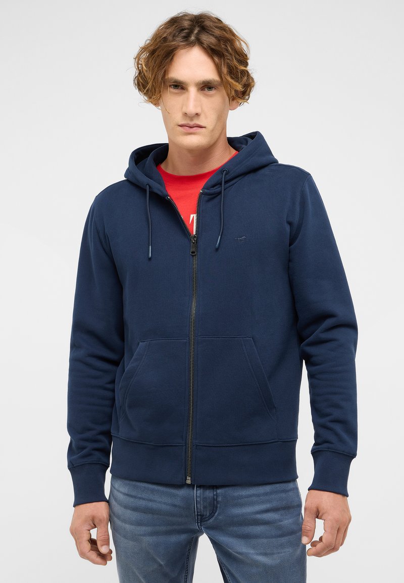 Marineblauer Kapuzenpullover mit Reißverschluss aus Baumwollmischung, mit Fronttasche, Kordelzugkapuze sowie gerippten Bündchen und Saum. Über einem roten Shirt getragen.