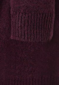 Gebreide trui in diep bordeauxrood, met een zachte textuur, geribbelde manchetten en decoratieve stiksels. Stof lijkt warm en comfortabel.