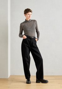 Černé kalhoty s vysokým pasem, černým opaskem a chunky černými kotníkovými botami. Top má přiléhavý střih s vlnitým pruhovaným vzorem v béžové a černé barvě.