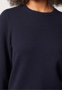 Granatowy sweter wykonany z miękkiej dzianiny, z okrągłym dekoltem i długimi rękawami zakończonymi prążkowanymi mankietami.