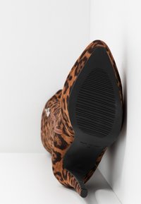 Zapato de tacón alto de piel de ante con estampado de leopardo, con puntera afilada, suela delgada de goma negra y una cremallera decorativa en el lado.