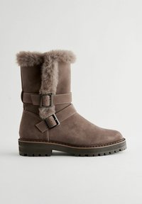 Brown suede ankle boot with faux fur trim and two adjustable buckles. Chunky rubber sole with textured tread for grip.