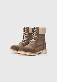 Bottines en daim marron avec un laçage à l'avant, un col rembourré et une semelle en caoutchouc de couleur claire. Caractéristiques : détails de couture et fermeture éclair sur le côté.