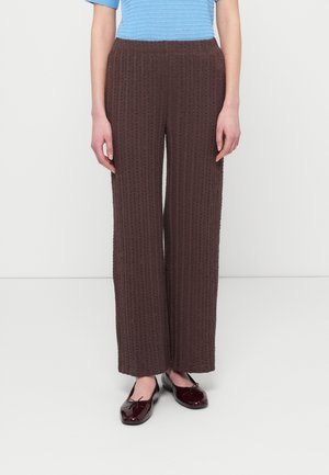 Brune bukser med vide ben og tekstureret mønster, med elastik i taljen og en løs pasform. Kombineret med bordeaux flade sko.