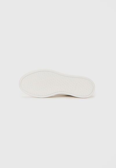 Suola di una sneaker bianca con un sottile motivo circolare sul battistrada, mostrata su uno sfondo bianco uniforme.
