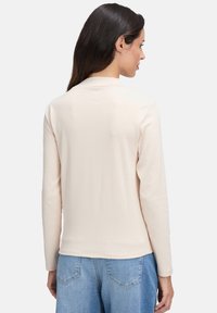 Beige Langarmoberteil mit rundem Ausschnitt. Weicher Stoff und minimalistischem Design, kombiniert mit hellblauen Jeans.