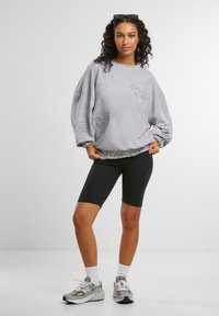 Gray oversized sweatshirt with textured butterfly design, paired with black bike shorts and gray athletic shoes. Smooth fabric, relaxed fit.