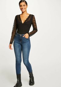 Maglietta nera a maniche lunghe con dettagli in pizzo e scollatura profonda a V, abbinata a jeans blu aderenti e stivaletti neri alla caviglia. Tessuto morbido, stile casual.
