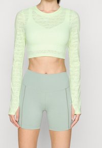 Light green long-sleeve crop top with repeating "NIKE PRO" logo; paired with high-waisted, pale green athletic shorts with stitch detailing.
