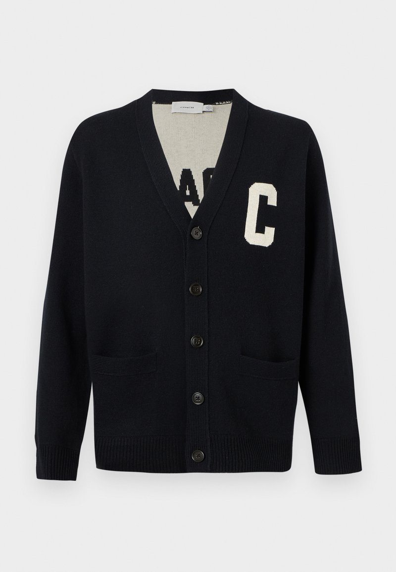 Cardigan noir boutonné avec col en V, deux poches avant, poignets et ourlet côtelés, et une grande lettre "C" blanche sur la poitrine gauche.