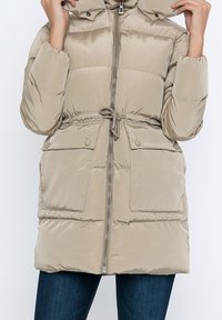 Beige Daunenjacke mit Reißverschluss, verstellbarem Bund und zwei Fronttaschen. Sie hat eine abnehmbare Kapuze und eine weiche, glatte Textur.