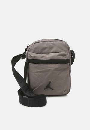 Gray nylon crossbody bag with a zippered front pocket, adjustable black strap, and black logo accent on the front. Compact and lightweight design.