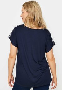 Mörkblå T-shirt med kort ärm och ett vitt mönster längs axlarna. Mjuk tyg, avslappnad passform, lätt drapering bak.