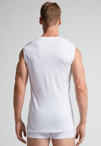 Biały męski t-shirt na ramiączkach bez rękawów, wykonany z bawełny, dopasowany fason o gładkiej fakturze, widok z tyłu, w zestawie z białymi slipami.