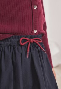 Maroon ribbed top with white buttons paired with a navy skirt featuring a red drawstring bow and gray metal tips, highlighting texture contrasts.