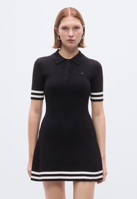 Melnas ribotas polo kleita ar īsām piedurknēm, ar baltām svītrām uz piedurknēm un apakšmalu. Klasisks apkakle ar pogas aizdari.