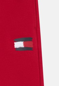 Rode stof met een horizontaal ontwerp van penseelstreken in zwart, wit en rood, geplaatst aan de zijkant van een kledingstuk.