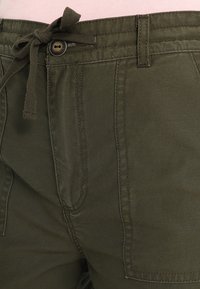 Olive green, casual trousers in durable fabric with a drawstring waistband and button closure, featuring front pockets and stitched details.