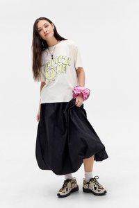 T-shirt grigio chiaro con una grafica a fumetto che dice "Squeeze Me!" abbinato a una gonna nera fluida e sneakers a fantasia. Accessorio scrunchie rosa.