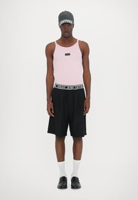 Rosa tank topp med et logo merke, kombinert med svarte shorts til knelengde med et merke rundt livet, hvite sokker og en grå caps.