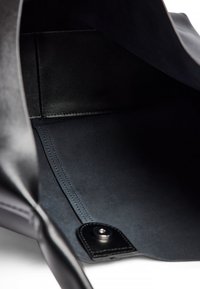 Schwarze Lederhandtasche mit glatter Innenausstattung; verfügt über ein elegantes Futter, kontrastierende Nähte und ein Druckknopfverschlussdetail.