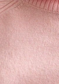 Lichtroze gebreide stof met een zachte textuur en een ribbelhalslijn. Het patroon is subtiel en gelijkmatig over het materiaal verdeeld.