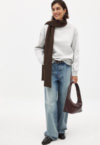 Grijze sweatshirt, bruine sjaal, lichtblauwe wijde jeans, zwarte schoenen en een bruin leren handtas met een soepele textuur en afgerond ontwerp.