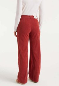Pantalones de pana rojos de pierna ancha con una cintura alta, tejido texturizado y una etiqueta posicionada en la parte posterior. Combinados con una camisa de manga larga.
