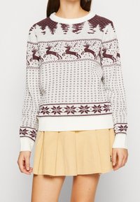 Pull en tricot blanc et bordeaux. Présente un motif festif avec des rennes, des arbres et des flocons de neige. Manches et ourlet côtelés, encolure ronde.