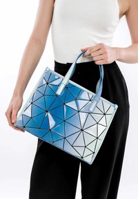 Zils ģeometrisks dizains auduma soma ar spīdīgu apdari, kas ir rotāta ar melni iezīmētām trīsstūrveida figūrām. Divas izturīgas rokturi ērta nēsāšanai.