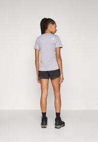 Grå kortermet t-skjorte med logo, kombinert med svarte shorts og svarte sko. Enkelt design, avslappet passform, egnet for atletiske aktiviteter.