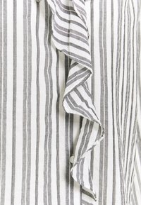 Tessuto a righe bianche e nere con bordo arricciato; presenta righe sottili e spesse, texture leggera e un dettaglio con bottone sul lato.