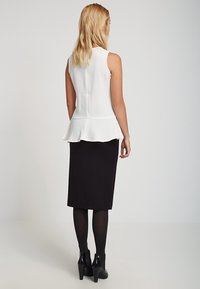 Top blanco con peplum y tela texturizada, combinado con una falda negra ajustada y botas negras hasta el tobillo. El conjunto tiene un aspecto elegante y moderno.