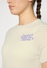 Light yellow t-shirt made of soft fabric, featuring a graphic text in purple that reads "THERE'S MORE OUT THERE" on the front.