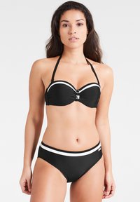 Zwart bikinitopje met een gevormde, straploze bovenkant met witte accenten en verstelbare bandjes. Hooggekruiste bottom met een brede witte band.