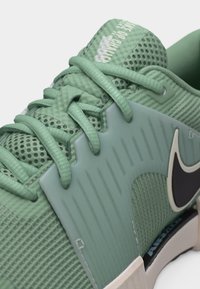 Chaussure de sport verte avec tige en mesh, panneau central texturé, lacets plats et logo Nike Swoosh noir sur le côté.