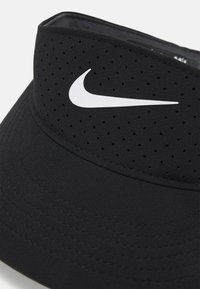 Črn vizir iz zračnega materiala, ki se ponaša s perforiranim trakom, ukrivljenim robom in belim logotipom Nike spredaj.