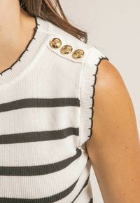 Débardeur en tricot blanc sans manches avec des rayures horizontales noires, des bords festonnés noirs et trois boutons décoratifs dorés sur l'épaule.