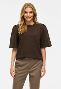 Brūns īsām piedurknēm tops ar noapaļotu kakla izmēru un puffed pleciem, izgatavots no gludas auduma. Apvienots ar pielāgotiem beigu atliktiem biksēm.