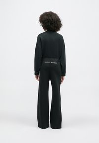 Czarny sportowy zestaw składający się z długiego rękawa i szerokich spodni. Charakterystyczne logo na pasku. Gładka tekstura i luźny krój.