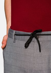 Szare spódnice w kratę z czarną elastyczną talią, zestawione z dopasowanym bordowym topem. Materiał jest gładki i ma wyraźnie zarysowany krój.