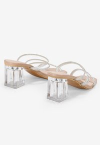 Sandalias de tacón bloque transparente con plantilla color nude, adornadas con múltiples tiras plateadas y brillantes strass, que presentan un tacón transparente.