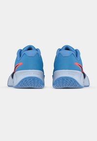 Ζευγάρι μπλε αθλητικά παπούτσια με λευκές μεσαίες σόλες και πορτοκαλί λεπτομέρειες, εμφανιζό�μενα από την πίσω πλευρά σε λευκό φόντο.