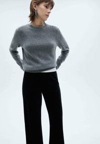 Maglione grigio corto in morbido tessuto con scollo rotondo, abbinato a pantaloni neri a vita alta e a gamba larga. Nessun motivo particolare.