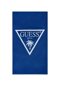 Asciugamano da spiaggia blu realizzato in tessuto morbido, con un logo triangolare bianco che presenta la scritta "GUESS" e un motivo con palma al centro.