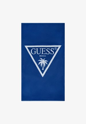 Asciugamano da spiaggia blu realizzato in tessuto morbido, con un logo triangolare bianco che presenta la scritta "GUESS" e un motivo con palma al centro.