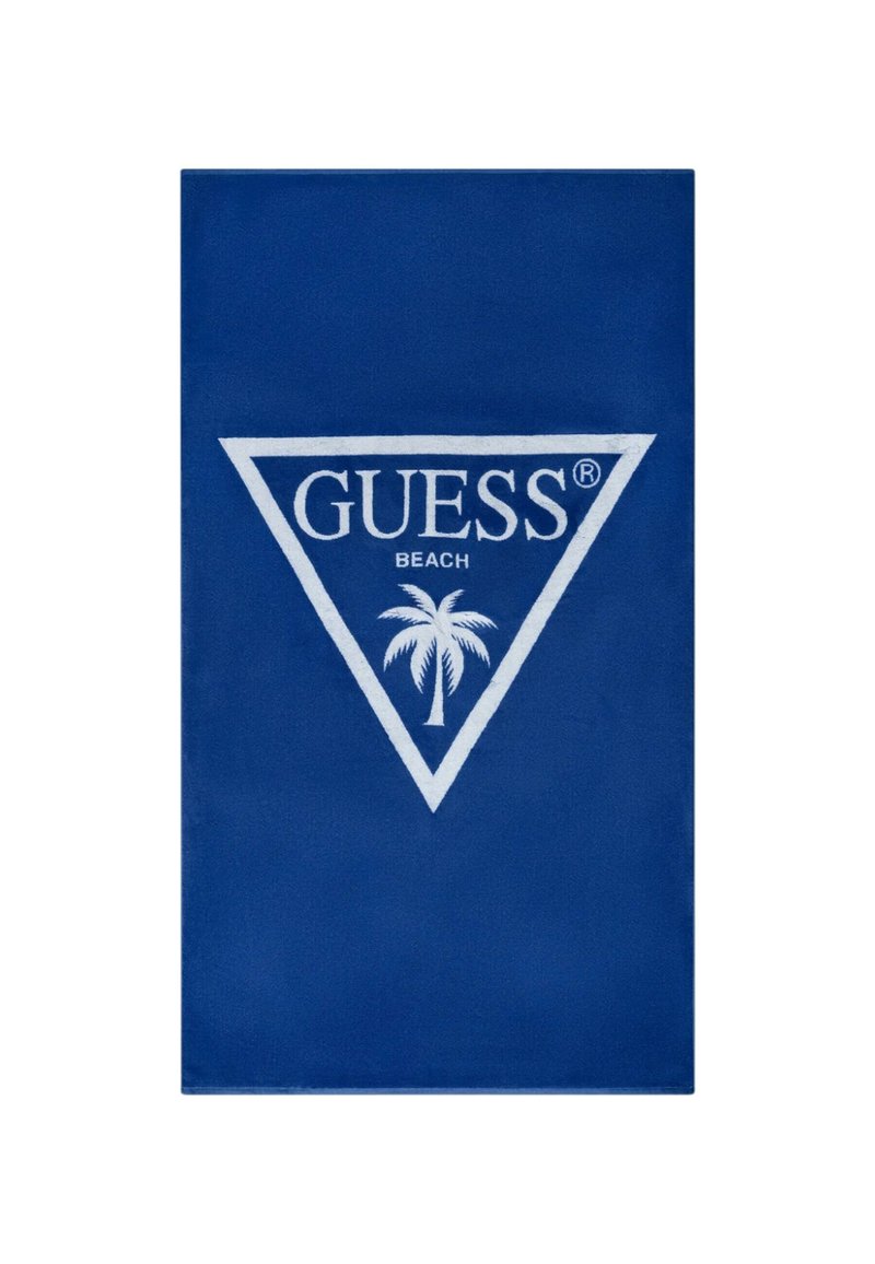 Asciugamano da spiaggia blu realizzato in tessuto morbido, con un logo triangolare bianco che presenta la scritta "GUESS" e un motivo con palma al centro.