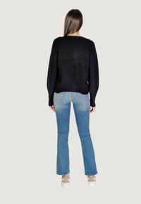 Schwarzer Pullover mit lockerer Passform, langen Ärmeln und rundem Ausschnitt, kombiniert mit hellblauen Schlagjeans und weißen Sneakers.