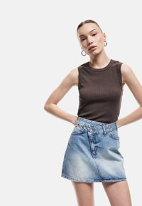 Braunes ärmelloses Oberteil, kombiniert mit einem hellblauen Denim-Minirock mit vorderen Taschen und sichtbaren Nähdetails.