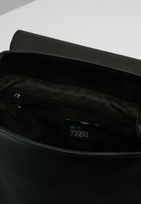 Bolso tote negro con un exterior de piel suave y un bolsillo interior con cremallera. Contiene una etiqueta con el nombre de la marca "even & odd."